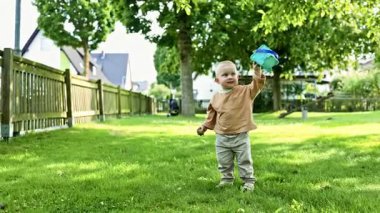 Parkta yeşil çimlerde koşan şık elbiseli, modern 2 yaşındaki bir çocuk. Parkta yürüyüş yapan bir çocuk. Sıcak ve güneşli bir günde parkta yürüyüş yapan kot pantolonlu ve tişörtlü bir çocuk..