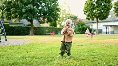 Parkta yeşil çimlerde koşan neşeli 2 yaşında bir çocuk. Çocuk parkta oyun oynuyordu. Neşeli çocuk dışarıda çimenlerde koşuyor. Çocuk gelişimi.