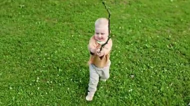 Parkta yeşil çimlerde koşan tişörtlü ve pantolonlu sevimli 2 yaşında bir çocuk. Sıcak bir yaz gününde yürüyüş yapan bir çocuk. Bebek yürüyüş sırasında eğleniyor ve gülümsüyor..