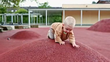 Küçük aktif çocuk oyun parkındaki tepelerde koşuyor. Çocuk koşuyor ve temiz havayı soluyor. Kot pantolonlu ve tişörtlü çocuk dışarıda oynuyor..