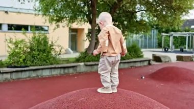 Küçük bir çocuk lastik kaplı bir oyun alanında koşuyor ve oynuyor. Çocuk temiz havada eğleniyor. Bir çocuk için sağlıklı bir yaşam tarzı. Yürüyen çocuk geliştirme.