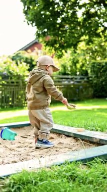 Anaokulunun dışındaki kum havuzunda oynayan iki yaşında bir çocuk. Sonbahar ceketi giymiş bir çocuk oyun bahçesinde oynuyor. Yürüyüş sırasında çocukların dışarıda yaptıkları..