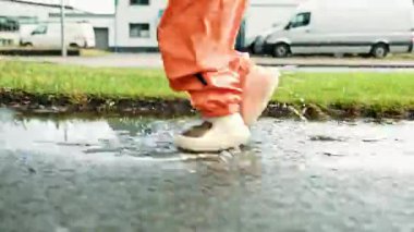 Su birikintilerinde koşan lastik çizmeli çocukların ayaklarına yakın çekim. Çocuk yağmurdan sonra su birikintilerinde koşuyor. 2 yaşında yağmurluk giymiş, botları su birikintilerinde koşan bir çocuk..