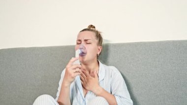 Hasta kadın evde öksürüyor yatakta oturuyor ve nebulizörle nefes alıyor. Solunum cihazıyla nefes almakta zorlanan bir kadın. Evde kendi kendine tedavi..