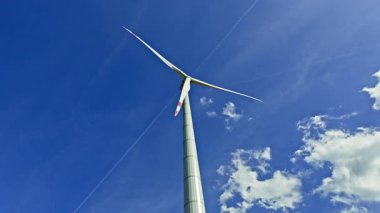 Arkaplanda bulutlu mavi gökyüzü olan büyük bir yel değirmeni. Parlak güneşli sonsuz gökyüzünün arka planında rüzgar türbini.