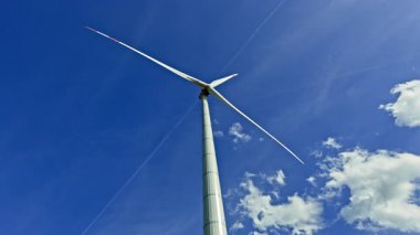 Arkaplanda bulutlu mavi gökyüzü olan büyük bir yel değirmeni. Parlak güneşli sonsuz gökyüzünün arka planında rüzgar türbini.