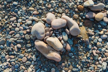 Çeşitli şekil ve boyutlarda pürüzsüz çakıl taşları sahili kaplıyor, güneşin altında parlıyor, ziyaretçileri doğanın güzelliğiyle bağlantı kurmaya ve duraklamaya davet eden doğal bir mozaik oluşturuyor..