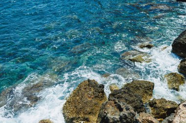 Parlak güneş ışığı, turkuaz suyu aydınlatır. Dalgalar kıyıdaki engebeli kayalara çarparak, rahatlama ve yansıma için mükemmel, doğanın güzelliğinin huzurlu bir sahnesini yaratır..