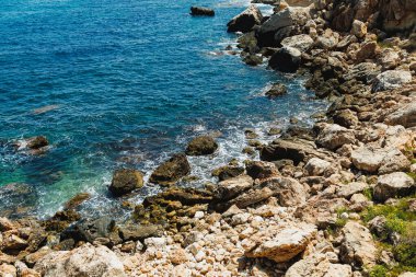 Okyanus parlak mavi bir gökyüzünün altında kayalık kıyılara nazikçe döner. Güneş ışığı suda parıldıyor. Bu huzurlu deniz kıyısında doğanın güzelliği aşikar..
