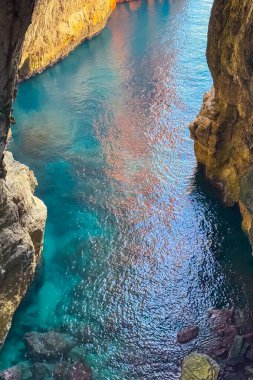Yükselen kayalıkların altında kristal berraklığında su yavaşça dar bir kanyondan akar. Güneş ışığı yüzeyde parıldıyor, aşağıdaki canlı renkleri ortaya çıkarıyor. Doğa bu huzurlu ortamda gelişiyor..