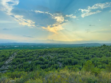 Altın ışınlar yumuşak bulutların arkasından çıkar, yemyeşil vadileri ve uzak tepeleri aydınlatır. Bu huzurlu akşamın sakinliği doğanın güzelliğini gözler önüne seriyor..