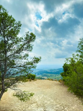 Dağın tepesinden nefes kesici bir manzara yükseliyor. Taze yeşil ağaçlar, kıvrılan bulutların altındaki geniş bir vadiye ulaşıyor. Gün ortası ihtişamıyla doğanın güzelliğini yakalıyor..