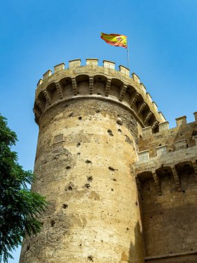 Valencia 'daki kule gibi bir yapı, parlak mavi bir gökyüzünün altında gururla duruyor, bu canlı şehirde tarih ve kültürün karışımını vurgulayan, nazikçe dalgalanan bir bayrak ile süslenmiş..