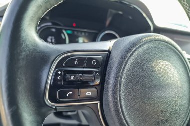 Bir el direksiyonu kavrar, telefon, ses ve ayarlar için çeşitli kontrollere erişir, parlak güneş ışığı altında çağdaş bir araçta sürmenin kolaylığını vurgular.