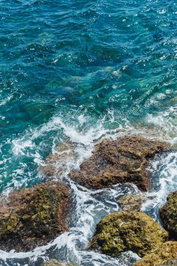 Okyanus dalgaları kıyı boyunca engebeli kayaları ritmik bir şekilde vurarak hareketli ve rahatlatıcı bir atmosfer yaratır. Güneş sudan yansıyarak denizin canlı mavilerini ve yeşilliklerini güçlendirir..
