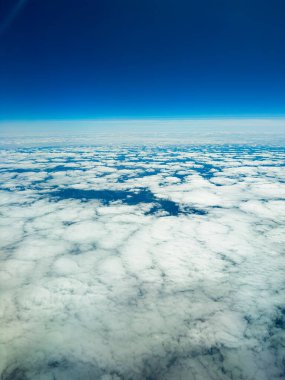 Ufuk boyunca uzanan yumuşak, beyaz bulutların göz kamaştırıcı manzarası canlı, mavi bir gökyüzünün altında. Sahne, Dünya 'nın doğal güzelliğine yukarıdan bir huzur ve merak uyandırıyor..