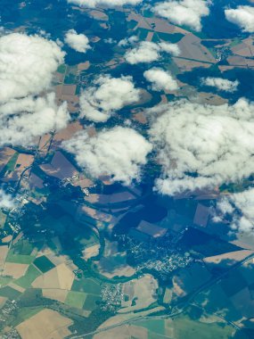 Yumuşak bulutlar, aşağıdaki yeşil tarlalar ve tarlaların karışımı üzerinde sürüklenir. Manzara, parlak mavi bir gökyüzünün altında canlı toprak ve yeşillikleri gösteriyor..