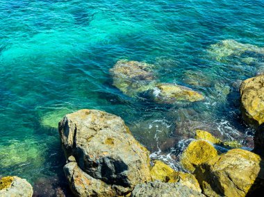 Güneş ışığı canlı turkuaz sulardan yansıyarak yüzeyin altındaki kayaları ortaya çıkarır. Huzurlu kıyı şeridi ziyaretçileri doğanın güzelliğinin ve sakin çevrenin tadını çıkarmaya davet ediyor..