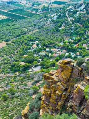 Kayalık bir uçurumdan, canlı ağaçlar ve meyve bahçeleri aşağıdaki vadiyi dolduruyor, manzaraya yerleşmiş sakin evlerin arkaplanlarına karşı doğanın ahengini sergiliyor..