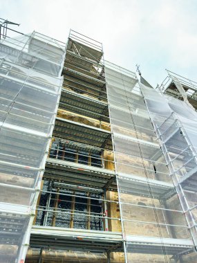 İskele, taş cephesini onarmaya hazırlanan işçilerin bulunduğu tarihi bir binayı kapsıyor. Şehrin serin bir gününde bulutlar tepemizde beliriyor..