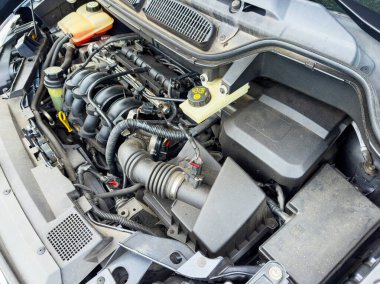 Bir araba motorunun yakın görüntüsü güneşli bir konumda bakım denetimi sırasında parçaların karmaşık düzenini, boruları, hortumları ve bileşenleri ortaya çıkarır..