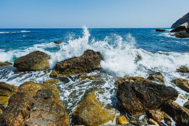 Sahil şeridi boyunca dalgaların ritmik bir şekilde çarpmasıyla berrak mavi su, resimli bir yerde huzurlu ama dinamik bir manzara yaratıyor..
