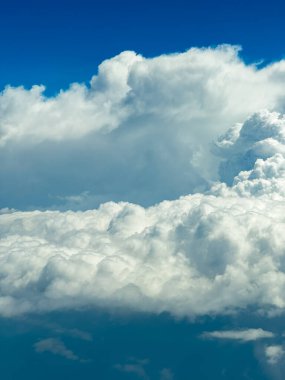 Kabarık beyaz bulutlar koyu mavi bir gökyüzüne karşı tembelce yüzerler. Güneş ışığı bulutların kenarlarını aydınlatıyor. Gün ortasında nefes kesici bir sükunet ve merak sahnesi yaratıyor..