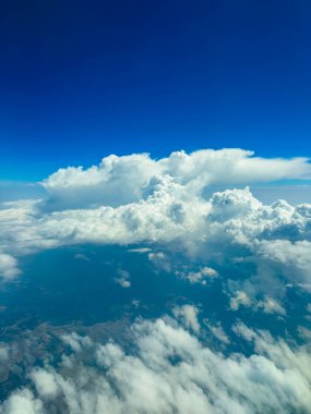 Yeryüzü ve gökyüzünün üzerinde, tüylü beyaz bulutlar, derin mavi bir zemin üzerinde sessizce süzülür, doğanın sükuneti ve ihtişamının çarpıcı bir görüntüsünü yaratır..
