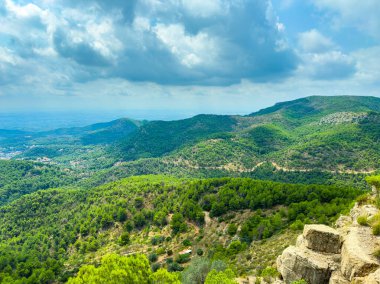 Bereketli yeşil tepeler dramatik bulutlu bir gökyüzü altında yavaşça yuvarlanır. Uzak dağlar güneş ışığıyla çerçevelenir. Bu barışçıl manzara doğanın güzelliğini keşfetmeye ve takdir etmeye davet ediyor..