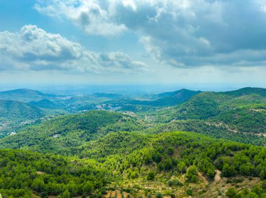 Kabarık bulutlarla dolu güzel bir gökyüzünün altında yemyeşil tepeler uzanır. Manzara, dağlık bölgenin canlı doğasını ve dinginliğini gösteriyor..