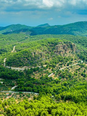 Parlak yeşillik kayan tepeleri kaplıyor, arazide bir yol labirenti dokuyor. Gökyüzü parçalı bulutlu, sakin bir atmosfer yaratıyor açık hava maceraları için mükemmel..