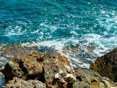 Turkuaz sular kayalık kıyı şeridine doğru yükselerek bu güzel sahil bölgesinde canlı bir manzara yaratıyor. Güneş dalgaları yansıtır, güne sıcaklık katar..