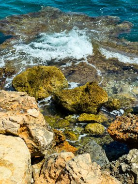 Sörf yavaşça antik kayalara çarpar ve kıyı boyunca bir ses senfonisi oluşturur. Güneş ışığı suda dans eder, bu kıyı manzarasının doğal güzelliğine hayat verir..