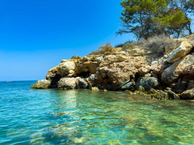 Kristal berrak sular engebeli kayalıklara çarparken, bereketli ağaçlar bu sakin sahil koyunda sıcak ve güneşli bir günde gölge oluşturur, dinlenmeye ve doğaya kaçmaya davet eder..