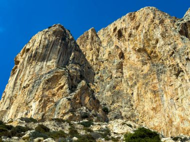 Uzun, engebeli uçurumlar, yeşil bitki örtüsüyle çevrili, keskin bir mavi gökyüzüne yükselir. Bu sakin ortamda doğanın gücünü ve görkemini vurgulayan çarpıcı bir kontrastlık yaratır..