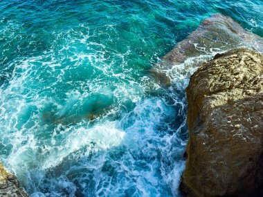 Parlak turkuaz sular engebeli kayaların etrafında döner ve berrak bir gökyüzü altında güzel bir manzara yaratır. Güneş ışığı okyanus yüzeyinde dans eder, huzuru ve huzuru davet eder..