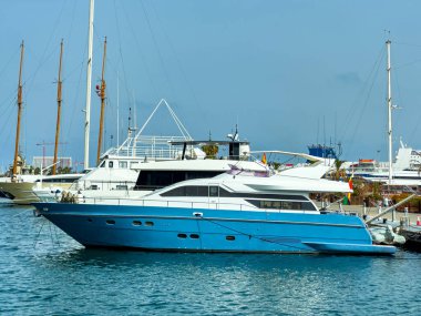Pürüzsüz mavi bir yat canlı bir marinada huzur içinde yatıyor. Açık mavi gökyüzünün altında diğer gemiler güneşli sıcaklıkla dolu güzel bir manzara yaratıyor..