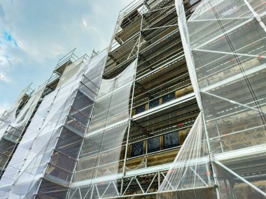 İşçiler, iskele ve koruyucu çarşafa sarılı eski bir binayı özenle restore ederek, işçilik ve tarihi koruma çabalarının bir karışımını sergilediler..