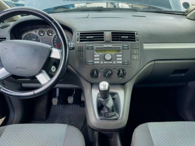 İyi bakımlı bir arabanın içinde şık bir direksiyon simidi, dijital bir gösterge paneli ve manuel vites kolu bulunur. Güneş ışığı, kabinin düzenli tasarımını vurgular.