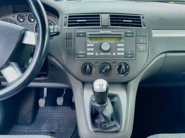 Küçük bir arabanın içinde, banliyö ortamında işlevsel ve modern bir tasarımı vurgulayan kontrol düğmeleri, radyo ve vites değişimi içeren temiz bir gösterge paneli sergilenir..