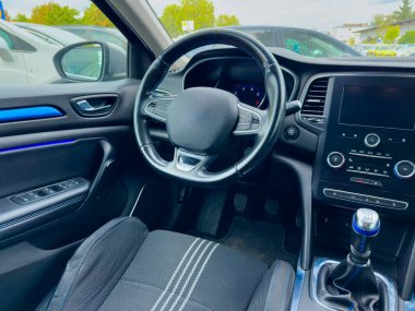 Gösterişli bir arabanın içinde, gösterge paneli dijital görüntüler ve düzenli kontroller içerirken, dışarıdaki hava hareketli bir park alanında bulutlu bir günde ipuçları verir..