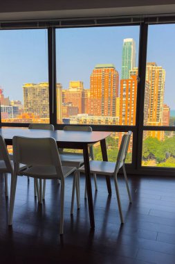 Parlak güneş ışığı çağdaş bir yemek alanını doldururken, parlak beyaz sandalyeler ve bir masayı aydınlatırken, gökdelenler büyük pencerelerin dışında görkemli bir şekilde yükseliyor, kentsel yaşamı gözler önüne seriyorlar..
