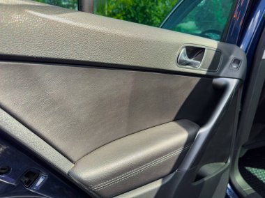 Bir araba kapısının parlak yüzeyi doğal güneş ışığı ile vurgulanır, yeşil zemine karşı yumuşak dokuları ve modern tasarımı vurgular, tazelik ve macera hissi yaratır..