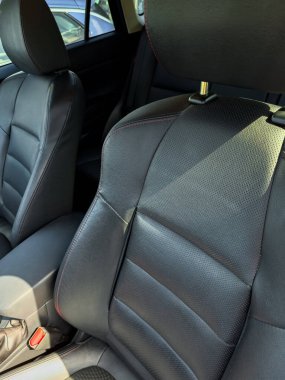 Siyah deri araba koltukları belirgin bir şekilde öne çıkarak, dokularını ve tasarımlarını ön plana çıkarıyor. Güneş ışığı koltuklarda parlıyor, iç mekanların kalitesini ve rahatlığını vurguluyor.