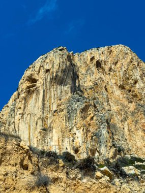 Kumlu toprağın üzerinde yükselen muhteşem kayalık bir uçurum, açık mavi gökyüzünün bir zeminine bakarak öğleden sonra güneşinin doğanın güzelliğini gözler önüne seriyor..