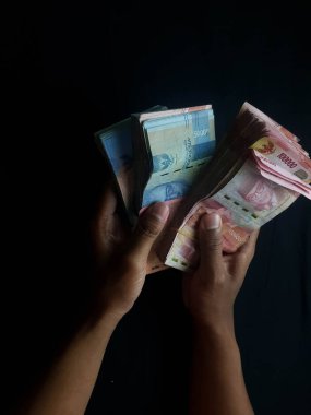 Milyonlarca rupiahı olan siyah bir arka planı olan kişi.