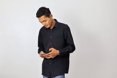 Lacivert tişörtlü Asyalı genç beyaz arka planda akıllı telefon kullanıyor.