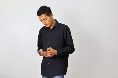 Lacivert tişörtlü Asyalı genç beyaz arka planda akıllı telefon kullanıyor.