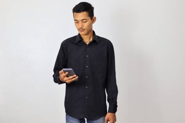 Lacivert tişörtlü Asyalı genç beyaz arka planda akıllı telefon kullanıyor.