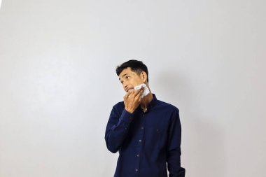 Genç Asyalı iş adamı beyaz arka plana yüzünü siliyor.